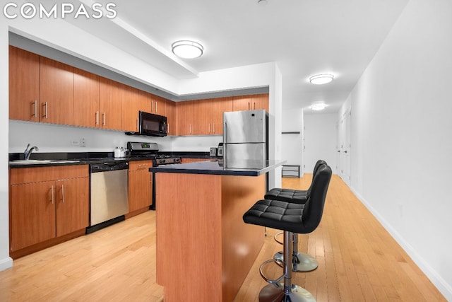 kitchen with appliances with stainless steel finishes, a kitchen island, light hardwood / wood-style flooring, a breakfast bar, and sink