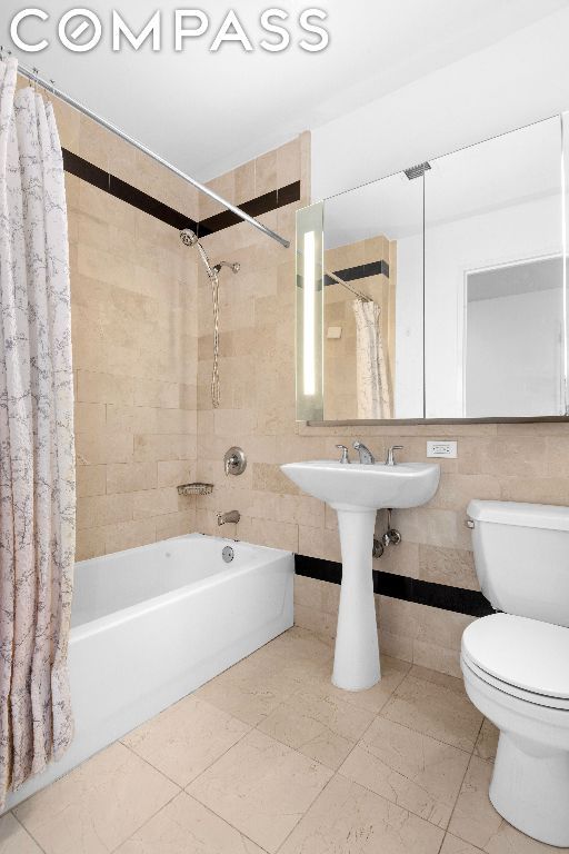 bathroom with toilet, tile walls, shower / bath combination with curtain, and tile patterned flooring