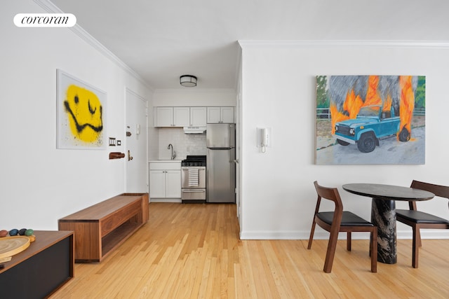 kitchen with a sink, backsplash, stainless steel appliances, white cabinets, and crown molding