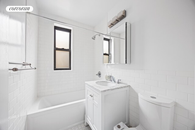 full bathroom with vanity, toilet, tiled shower / bath combo, and tile walls