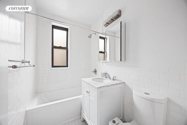 bathroom with a wainscoted wall, toilet, shower / bathing tub combination, tile walls, and vanity