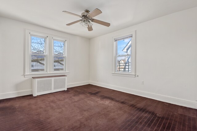 unfurnished room with dark carpet, radiator, ceiling fan, and baseboards