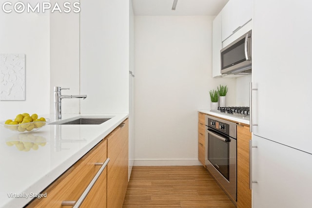 kitchen featuring light wood-type flooring, sink, stainless steel appliances, and white cabinetry