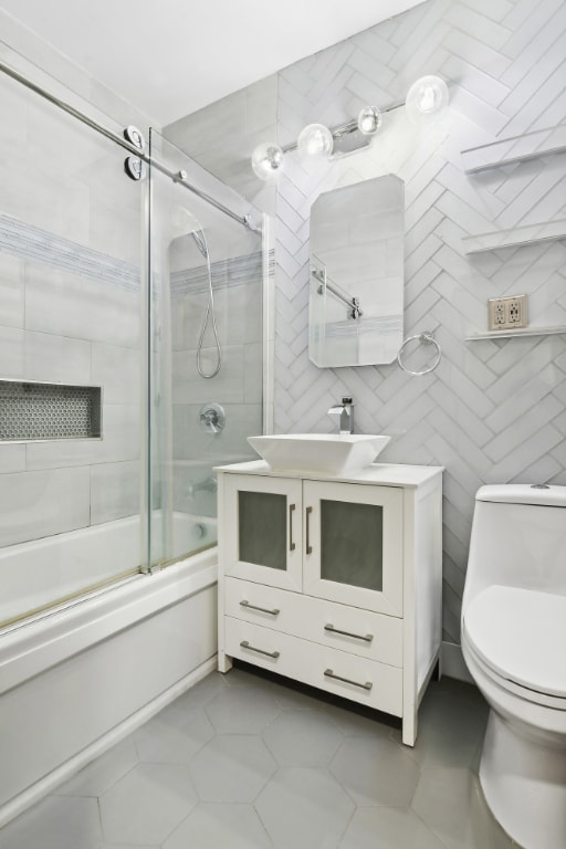 full bathroom with tile patterned flooring, enclosed tub / shower combo, toilet, tile walls, and vanity