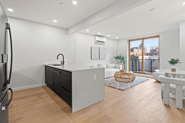 kitchen with light hardwood / wood-style floors, kitchen peninsula, stainless steel refrigerator with ice dispenser, an AC wall unit, and sink