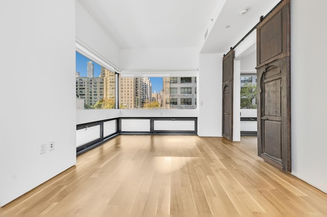 unfurnished room with a barn door, a city view, and light wood finished floors