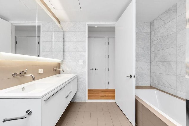 bathroom featuring tiled bath, tile walls, and vanity