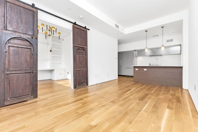 unfurnished living room with a barn door, sink, and light hardwood / wood-style floors