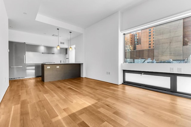 kitchen featuring decorative light fixtures, light hardwood / wood-style floors, decorative backsplash, and stainless steel refrigerator