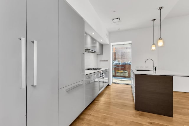 kitchen with dark brown cabinetry, tasteful backsplash, light hardwood / wood-style floors, sink, and hanging light fixtures