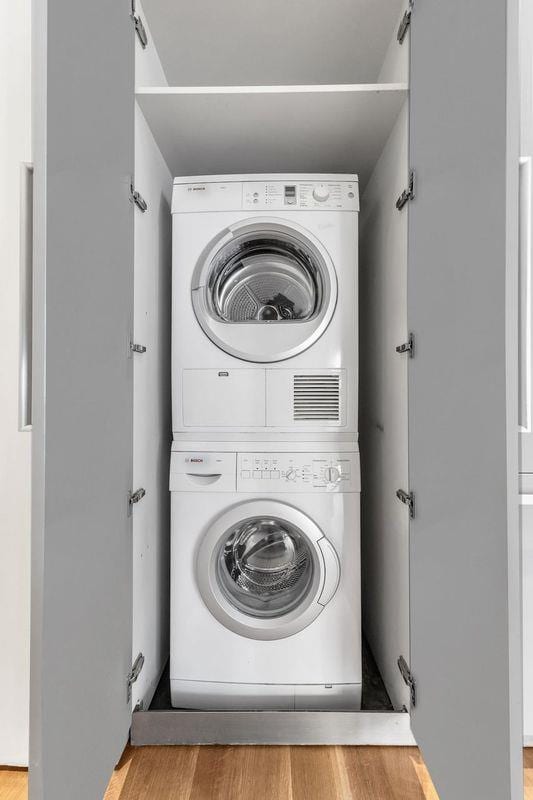 clothes washing area featuring stacked washing machine and dryer and wood finished floors
