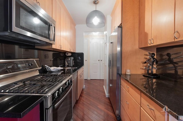 kitchen featuring stainless steel appliances, dark wood-type flooring, hanging light fixtures, dark stone counters, and sink