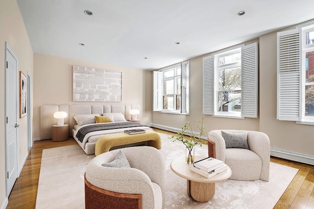 bedroom with a baseboard heating unit and light hardwood / wood-style flooring