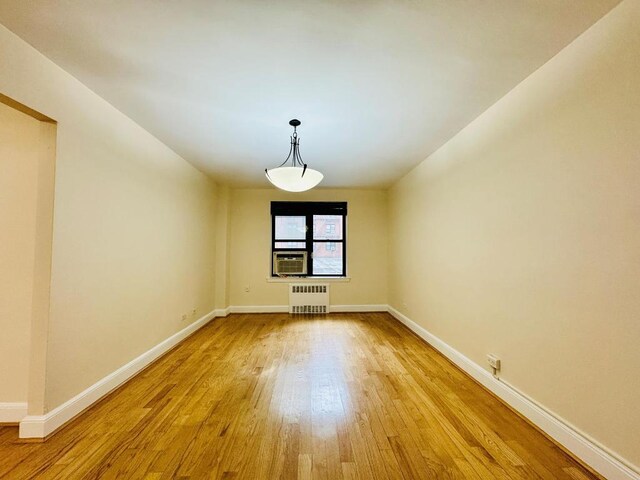 unfurnished room featuring cooling unit, radiator heating unit, and light hardwood / wood-style flooring