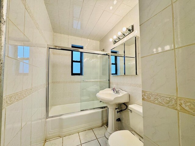 bathroom with tile patterned floors, toilet, tile walls, and bath / shower combo with glass door