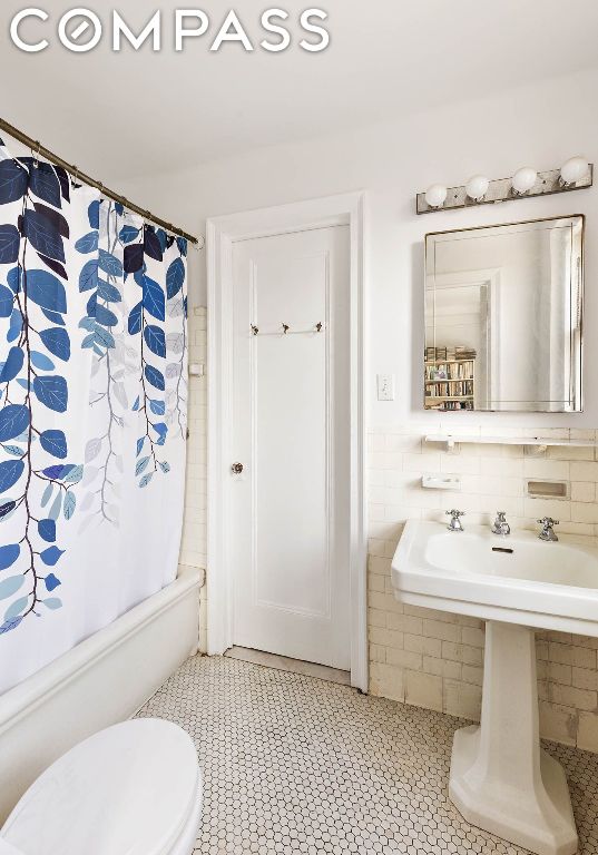 full bathroom featuring toilet, tile walls, tile patterned floors, shower / bathtub combination with curtain, and sink