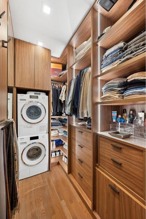 laundry area with stacked washing maching and dryer and light wood-type flooring