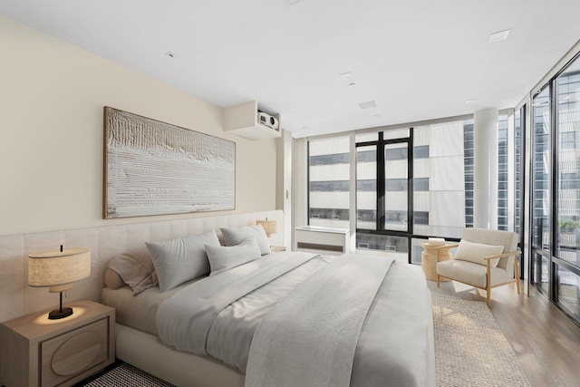 bedroom featuring access to exterior, a wall of windows, and wood finished floors