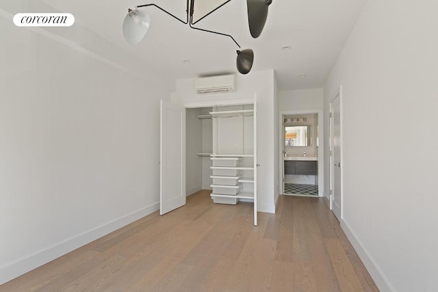 unfurnished bedroom with a closet, a wall unit AC, and light wood-type flooring