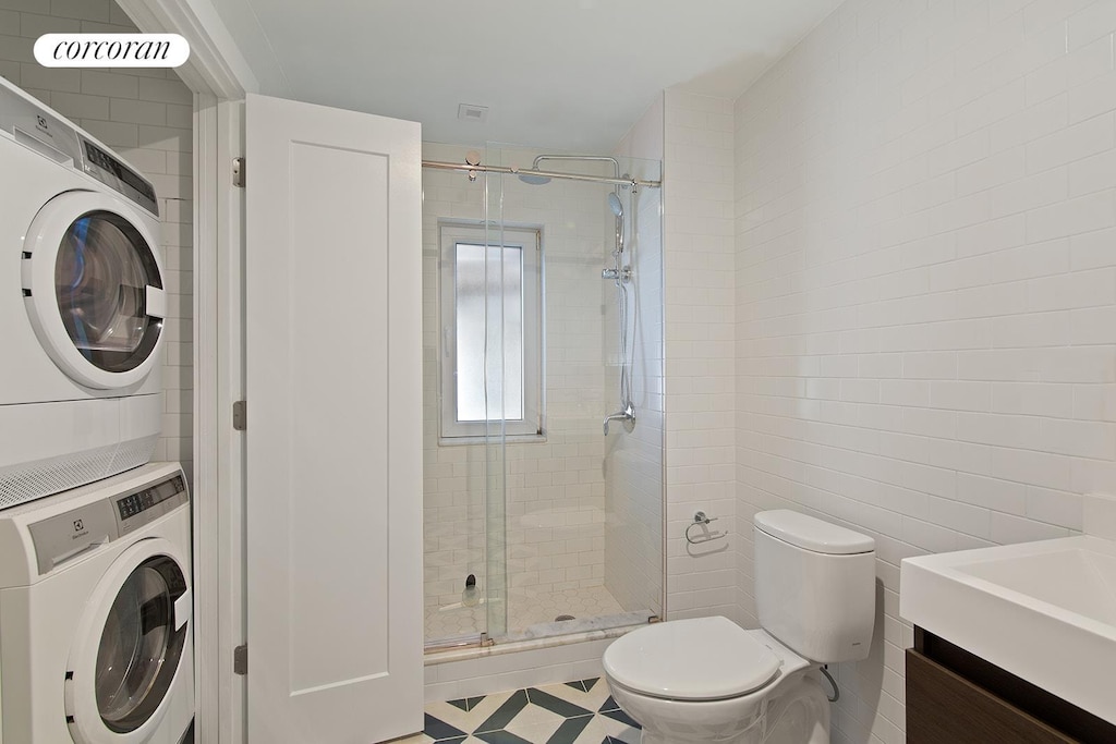 bathroom with tile walls, stacked washer and dryer, toilet, a stall shower, and vanity