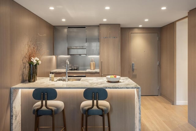 kitchen with sink, a kitchen bar, light stone counters, kitchen peninsula, and light wood-type flooring