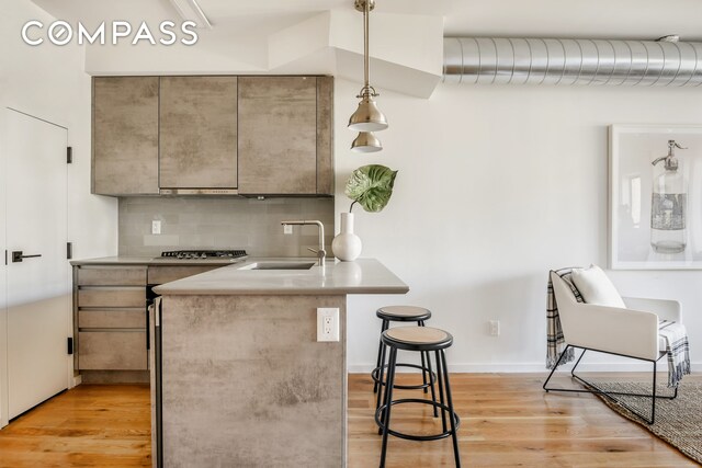 kitchen with stainless steel gas cooktop, sink, decorative light fixtures, a kitchen breakfast bar, and backsplash