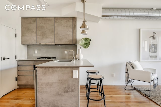 kitchen featuring light wood-style flooring, a sink, a kitchen breakfast bar, tasteful backsplash, and stainless steel gas stovetop