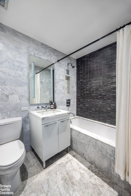 full bathroom with tile walls, toilet, vanity, and shower / bath combo