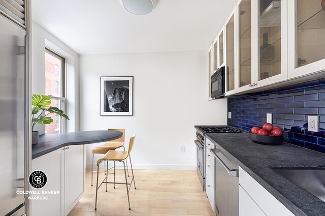 kitchen with tasteful backsplash, sink, light wood-type flooring, stainless steel appliances, and white cabinets