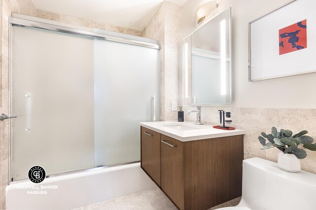 full bathroom with tile walls, toilet, vanity, and combined bath / shower with glass door