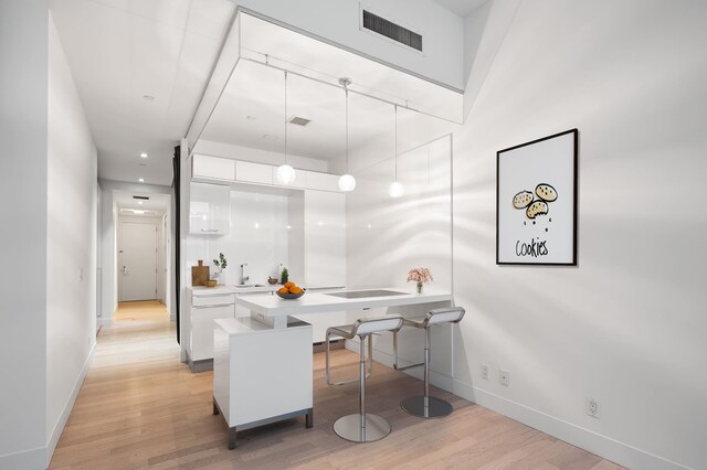 kitchen with light wood finished floors, visible vents, white cabinets, a breakfast bar area, and light countertops