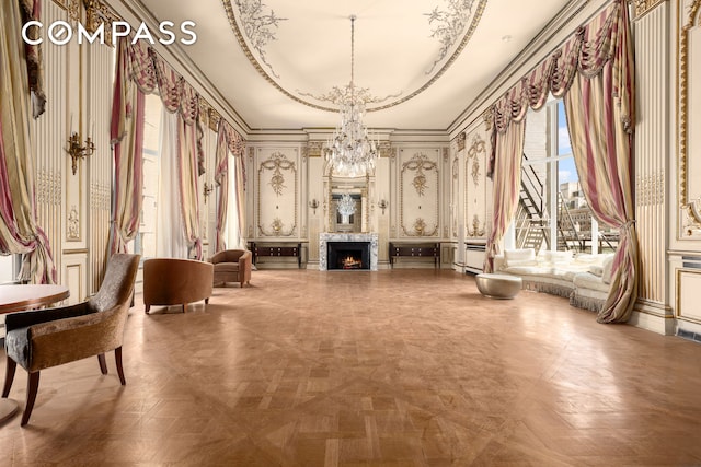 living area featuring baseboards, a raised ceiling, an inviting chandelier, and a warm lit fireplace