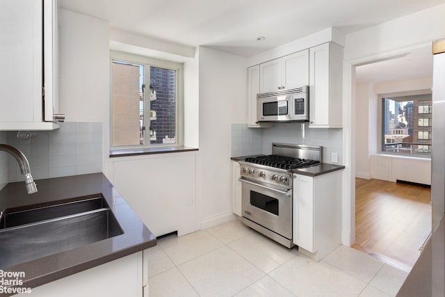 kitchen with appliances with stainless steel finishes, dark countertops, a sink, backsplash, and white cabinets
