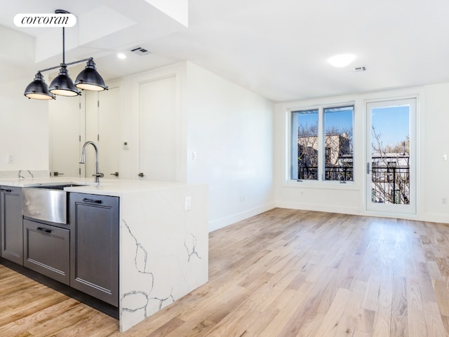 bar featuring sink, gray cabinetry, light stone counters, light wood-type flooring, and pendant lighting