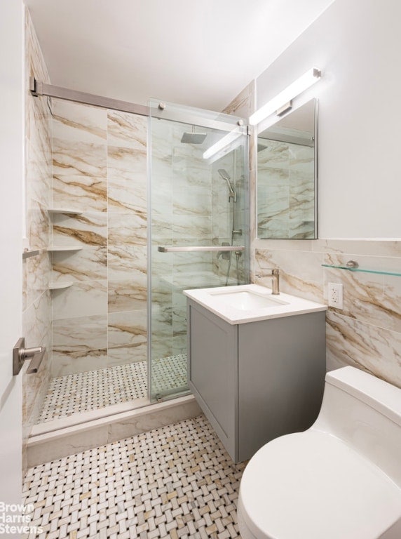 bathroom featuring toilet, tile walls, a shower with shower door, and vanity