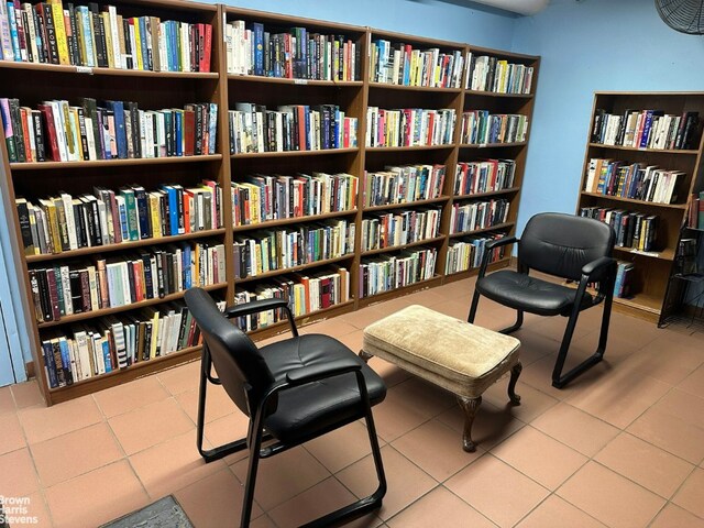 sitting room featuring wall of books and light tile patterned floors