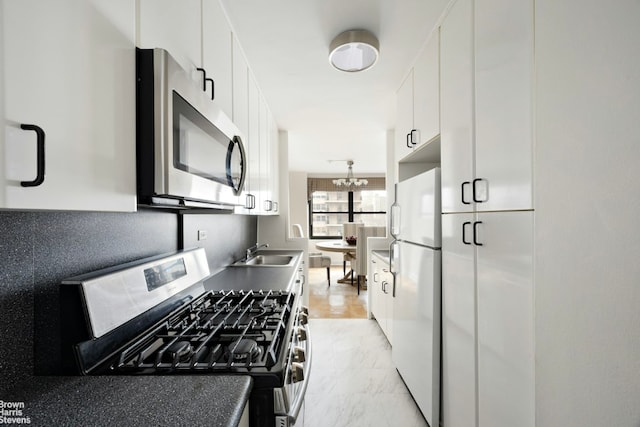 kitchen with marble finish floor, dark countertops, appliances with stainless steel finishes, white cabinets, and a sink