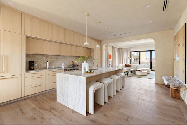 kitchen featuring light stone countertops, a kitchen bar, light wood-style floors, arched walkways, and modern cabinets