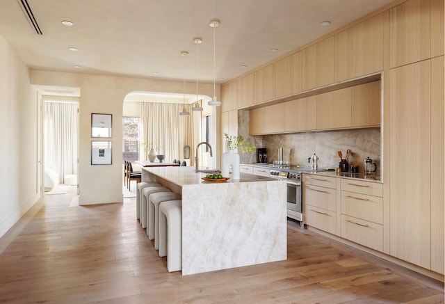 kitchen featuring stainless steel range with electric stovetop, an island with sink, modern cabinets, and light wood-style flooring