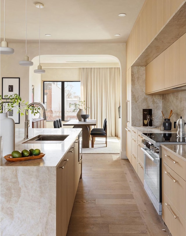 kitchen with backsplash, light wood-type flooring, stainless steel range with electric cooktop, modern cabinets, and a sink