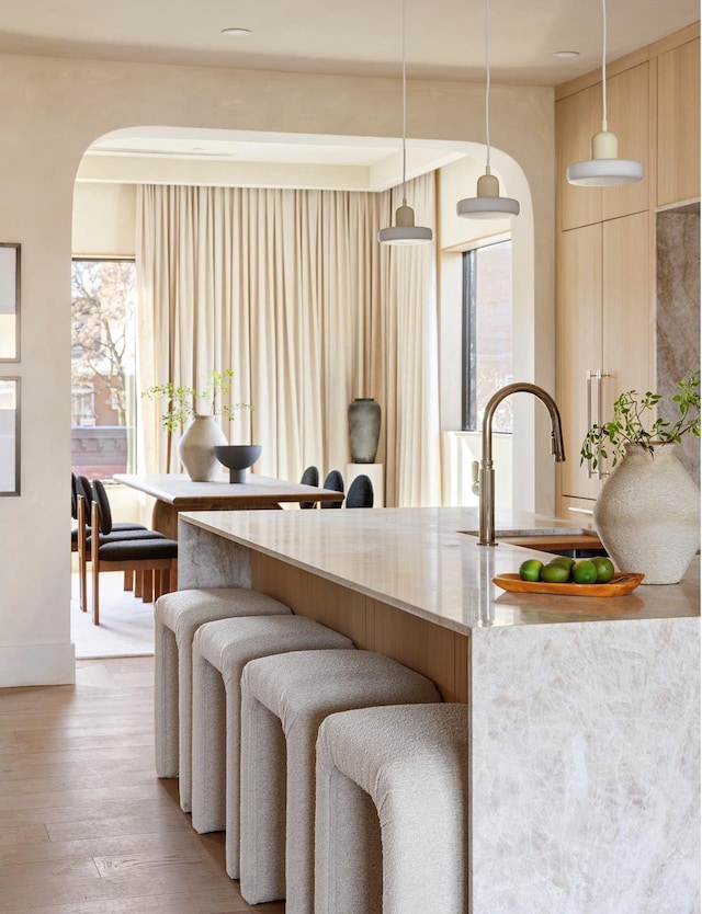 kitchen with light wood-style flooring, light brown cabinets, a sink, decorative light fixtures, and light stone counters