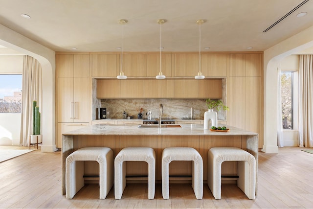 kitchen with a sink, light wood-type flooring, a kitchen breakfast bar, and backsplash