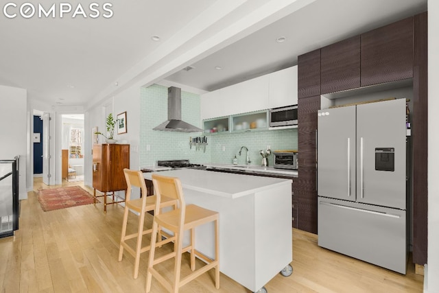 kitchen featuring white cabinetry, a kitchen island, white fridge with ice dispenser, decorative backsplash, and wall chimney range hood