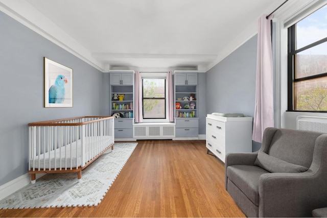 bedroom featuring radiator heating unit, a nursery area, and light hardwood / wood-style flooring