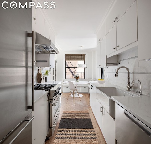 kitchen featuring light parquet flooring, range hood, white cabinetry, hanging light fixtures, and stainless steel appliances