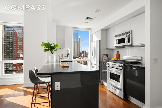 kitchen with dark countertops, appliances with stainless steel finishes, a breakfast bar, a city view, and a sink