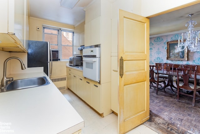 kitchen with wallpapered walls, radiator heating unit, ornamental molding, a sink, and white oven