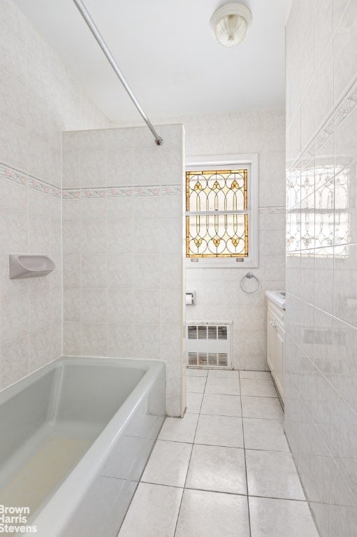 bathroom with a tub to relax in, tile patterned floors, tile walls, and vanity