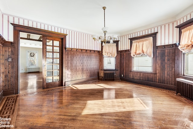 unfurnished dining area with radiator, hardwood / wood-style flooring, and a chandelier