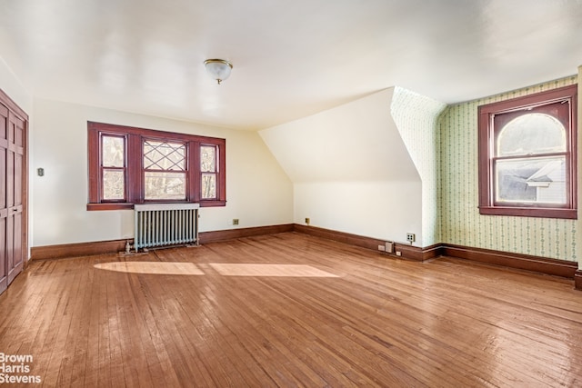 additional living space with hardwood / wood-style flooring and radiator heating unit